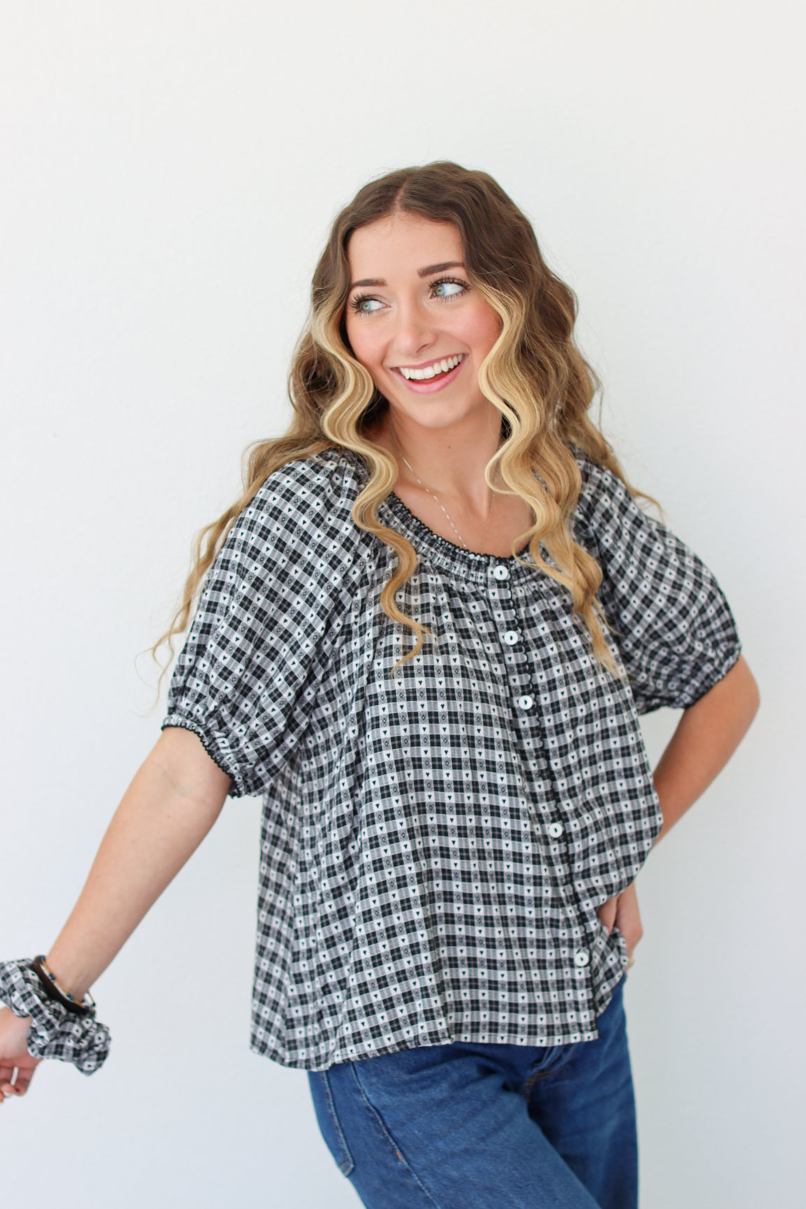 Woman wearing a black and white checkered shirt with blue jeans on a plain background