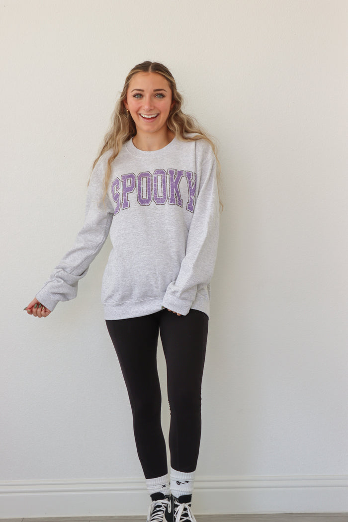 girl wearing light gray crewneck with purple "spooky" graphic