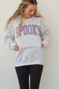 girl wearing light gray crewneck with purple "spooky" graphic