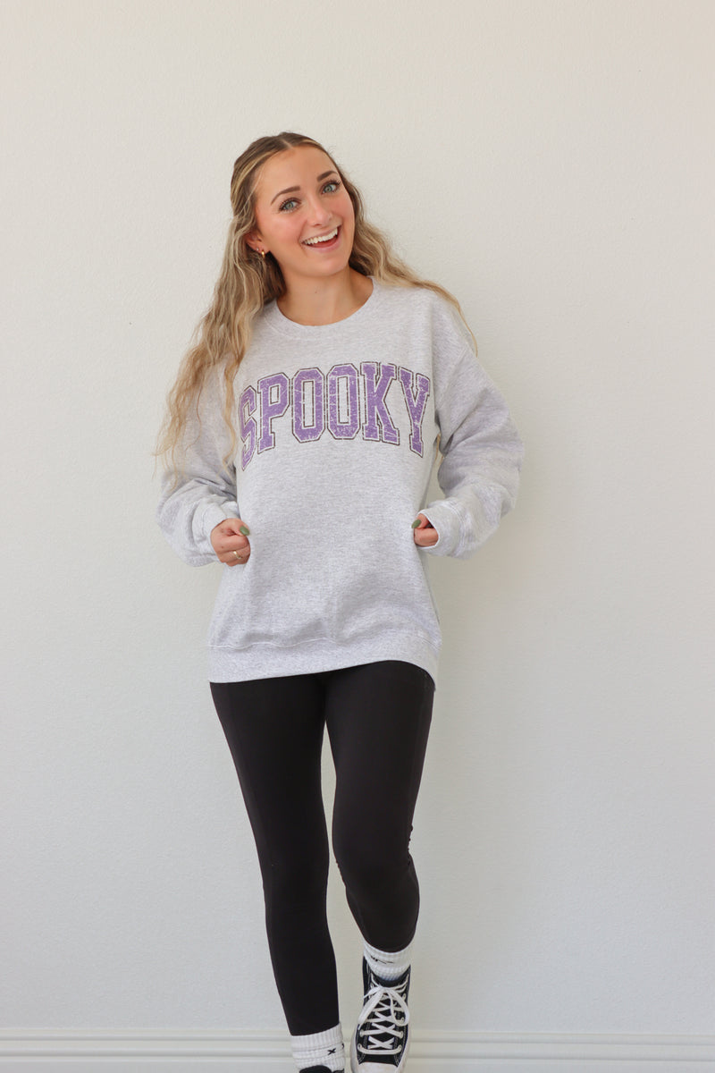 girl wearing light gray crewneck with purple "spooky" graphic