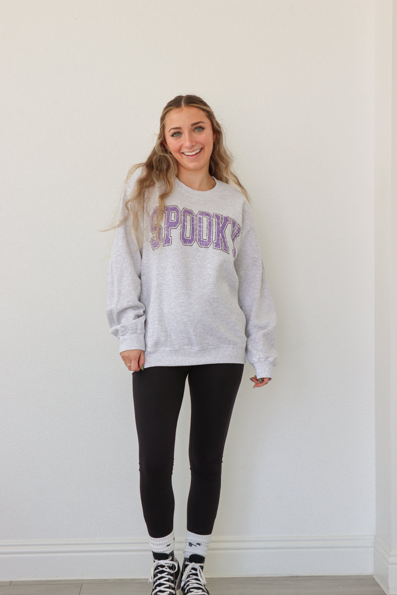 girl wearing light gray crewneck with purple "spooky" graphic