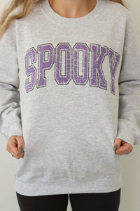 girl wearing light gray crewneck with purple "spooky" graphic