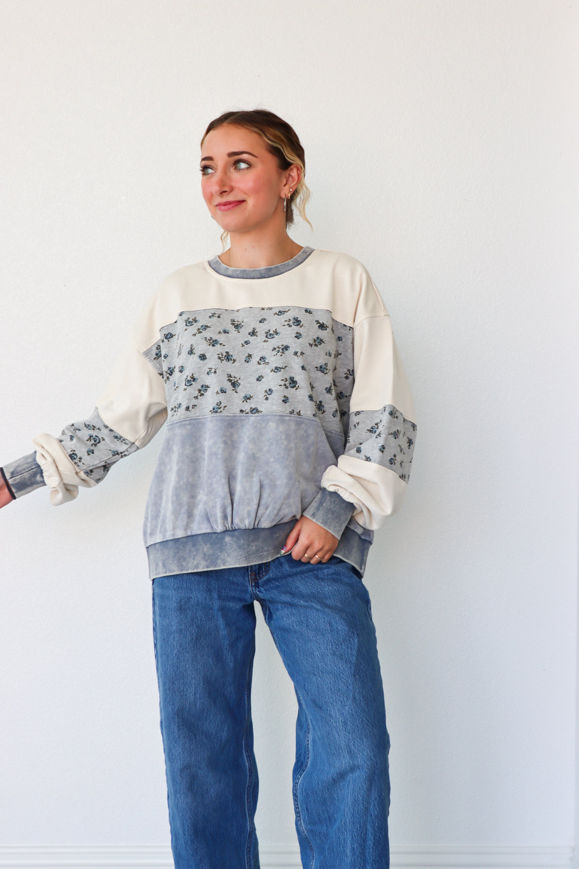 Woman wearing a color-blocked sweater with floral sleeves against a plain background