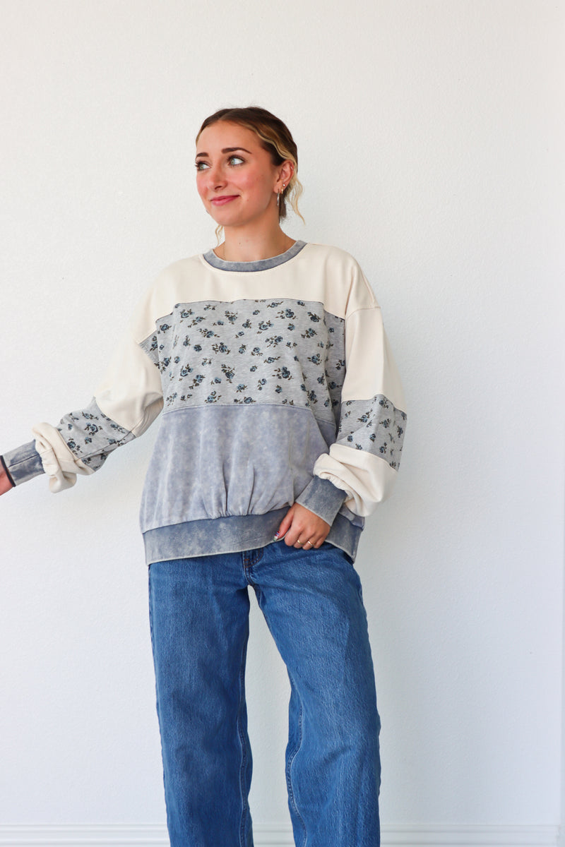 Woman wearing a color-blocked sweater with floral sleeves against a plain background