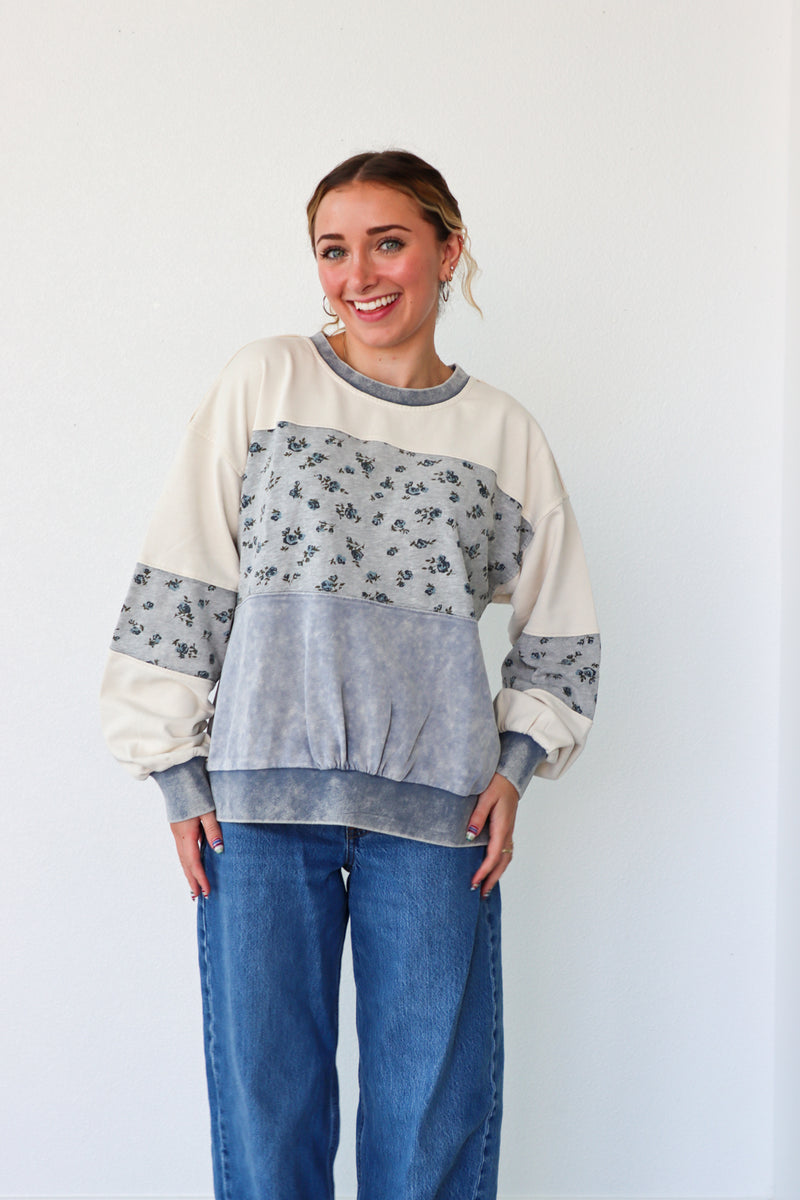 Woman wearing a color-blocked sweater with floral patterns on a plain background