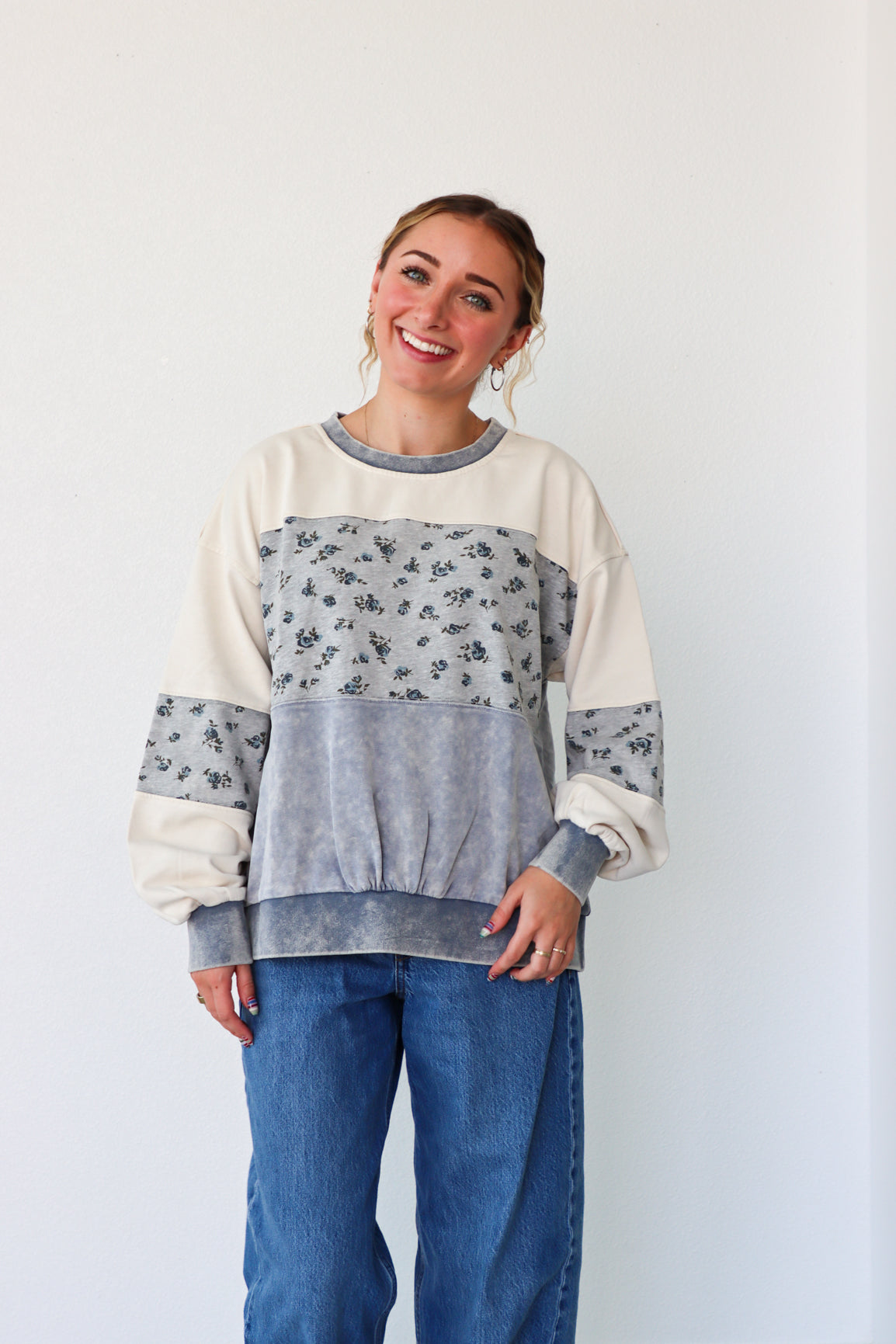 Woman wearing a color-blocked sweater with floral sleeves against a plain background