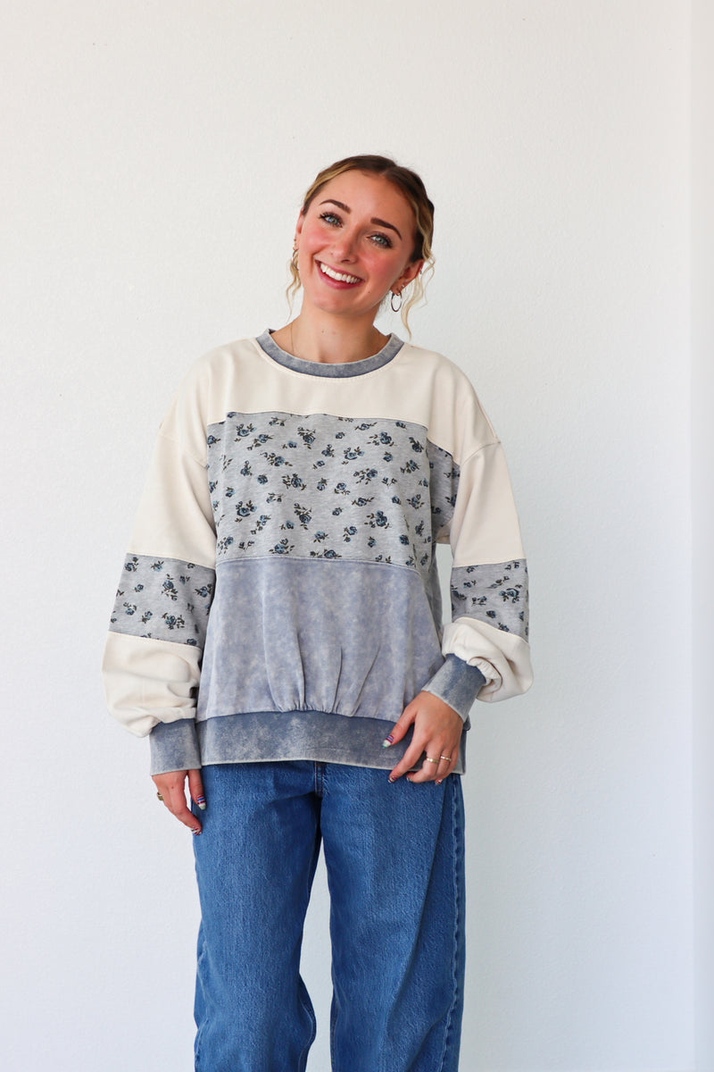 Woman wearing a color-blocked sweater with floral sleeves against a plain background