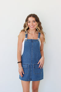 Woman wearing a denim overall dress against a white background