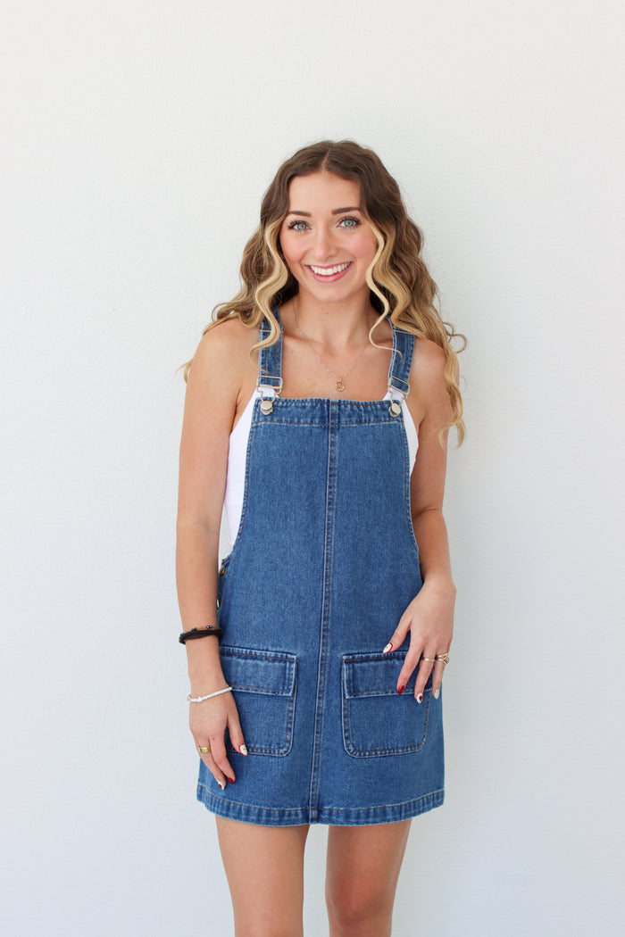Woman wearing a denim overall dress against a white background