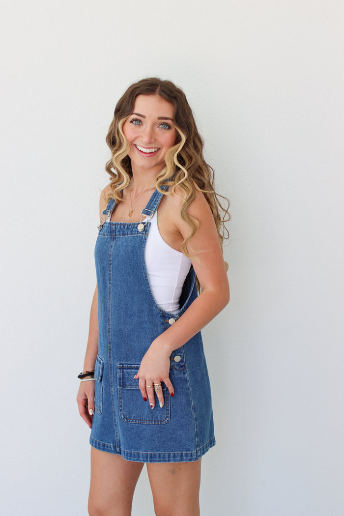 Woman wearing a denim overall dress against a white background