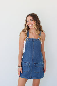 Woman wearing a denim overall dress against a white background