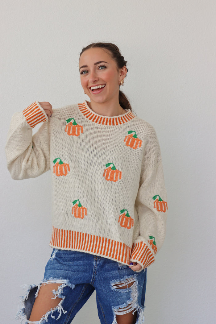 girl wearing cream sweater with orange pumpkin design