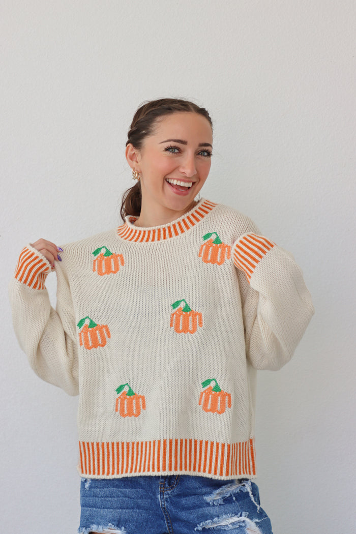 girl wearing cream sweater with orange pumpkin design