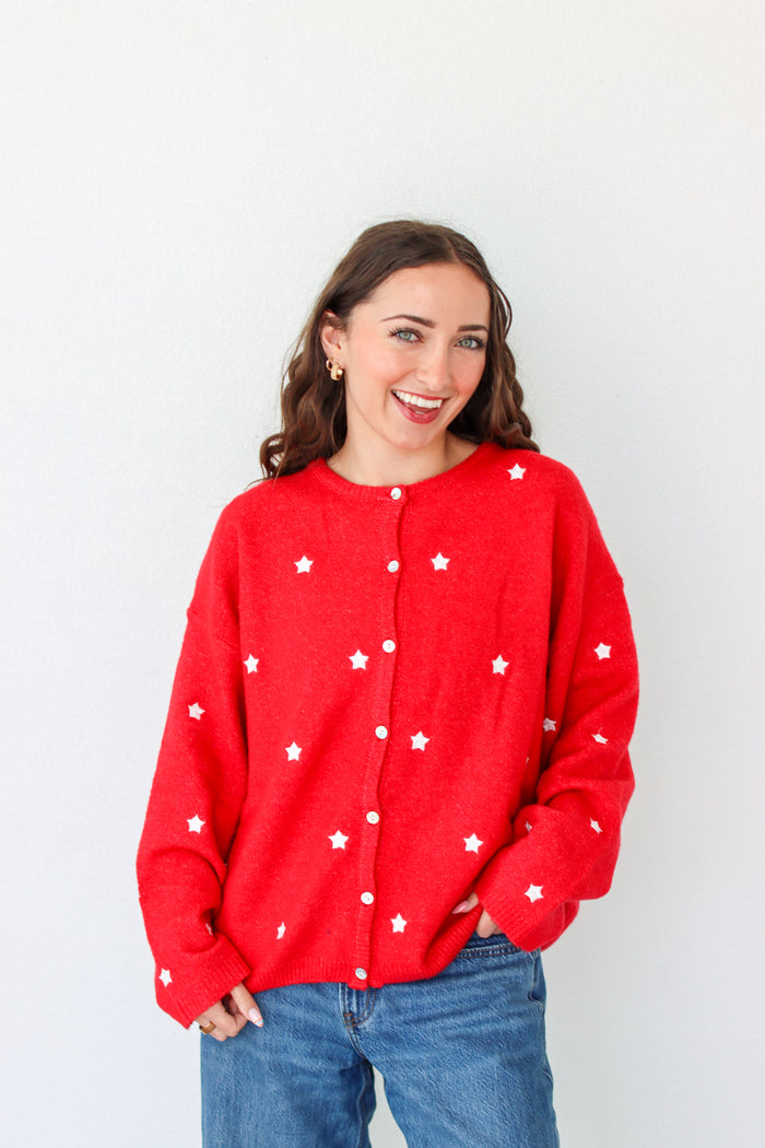 Woman wearing a red cardigan with white star patterns against a plain background