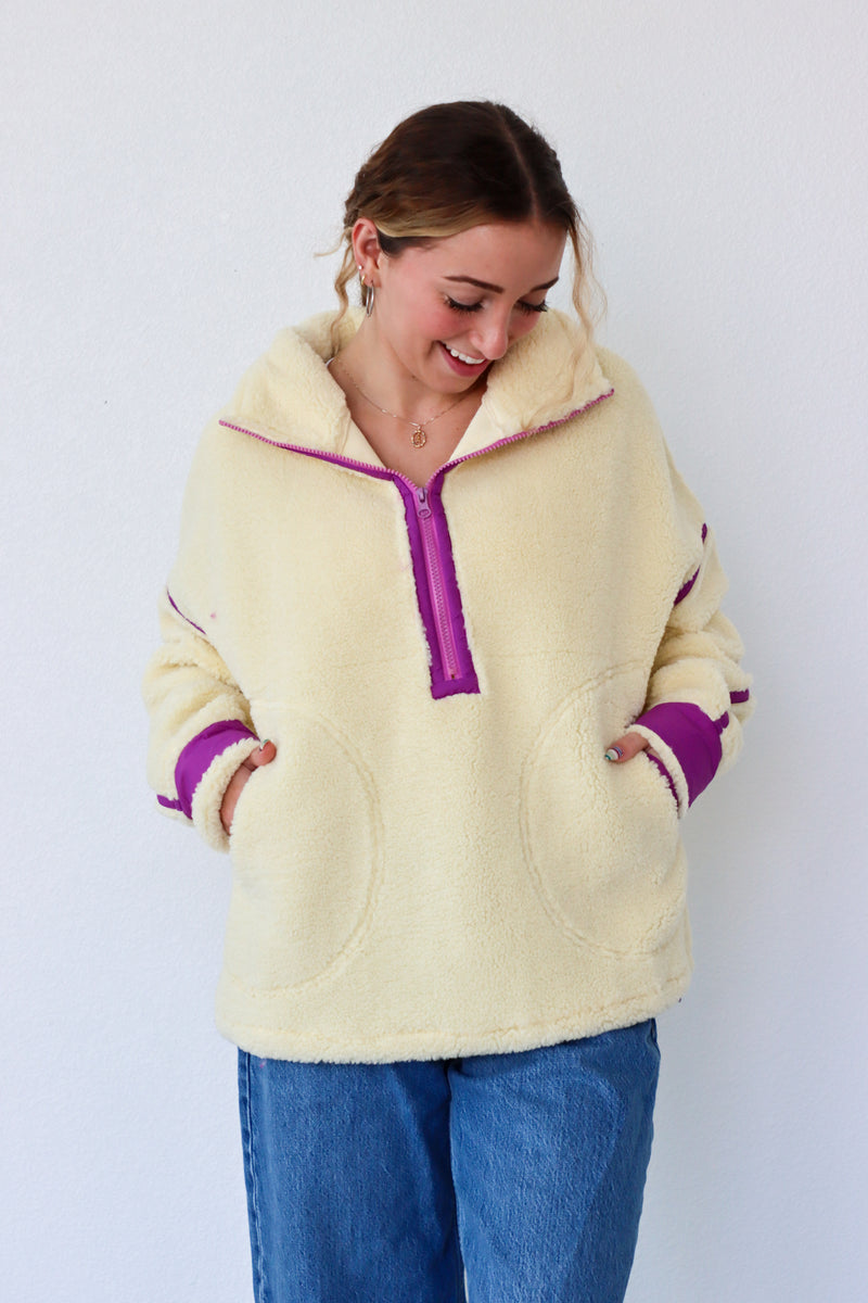 Woman wearing a cream fleece pullover with purple accents against a white background