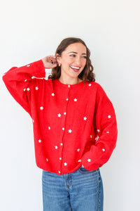 Woman wearing a red cardigan with white star patterns against a plain background