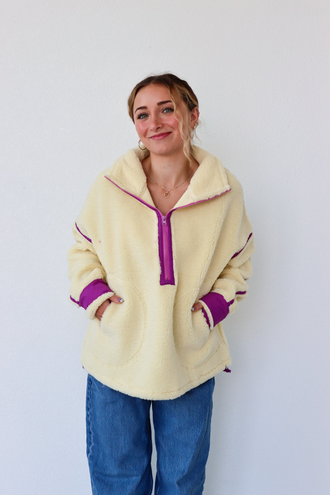 Woman wearing a cream fleece pullover with purple accents against a white background