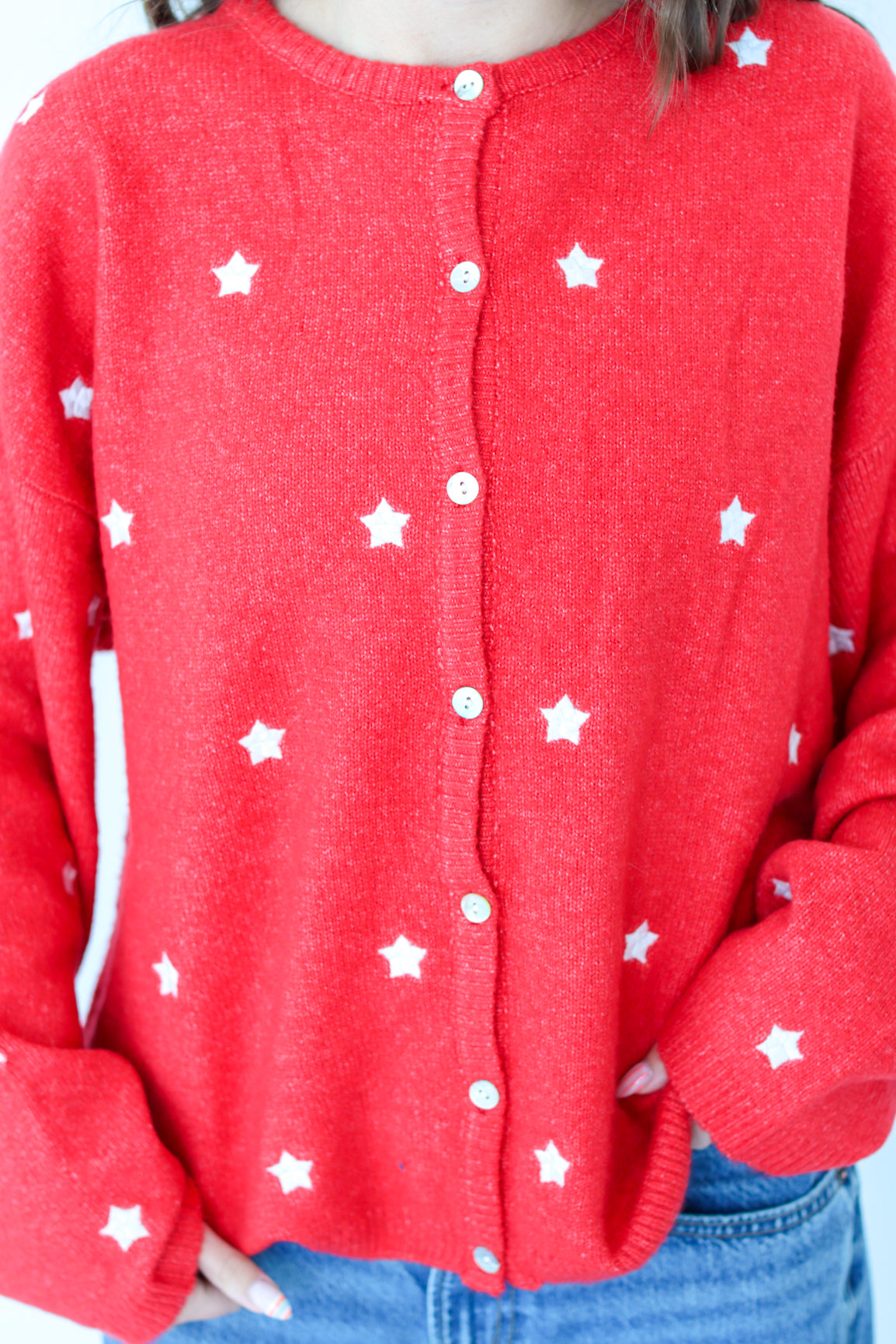 Red cardigan with white star patterns worn by a person, with a plain background