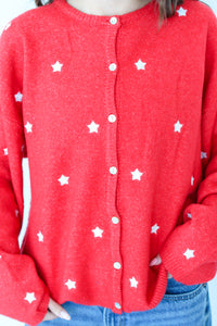 Red cardigan with white star patterns worn by a person, with a plain background