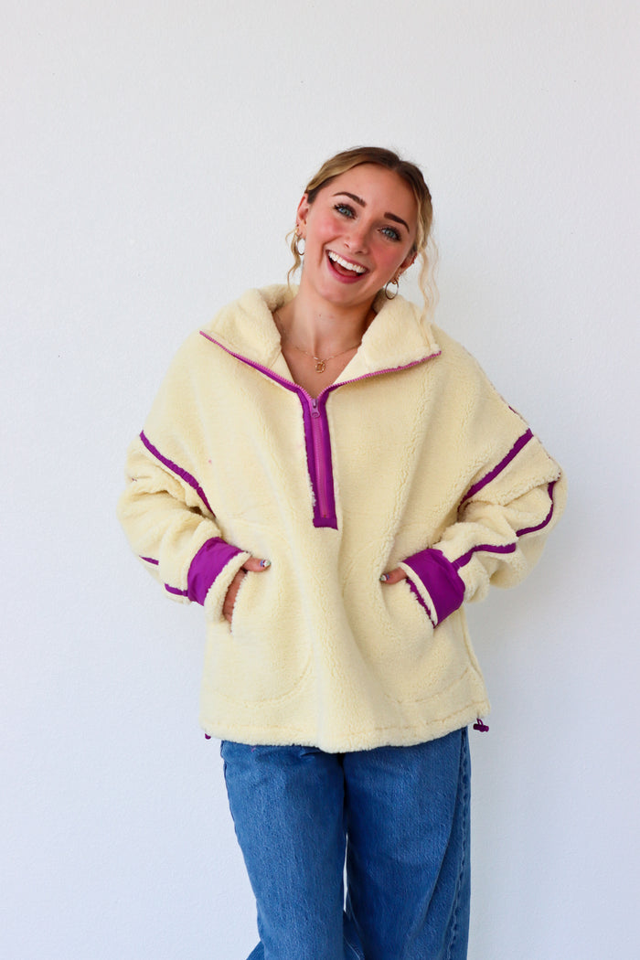 Woman wearing a cream fleece pullover with purple trim against a white background