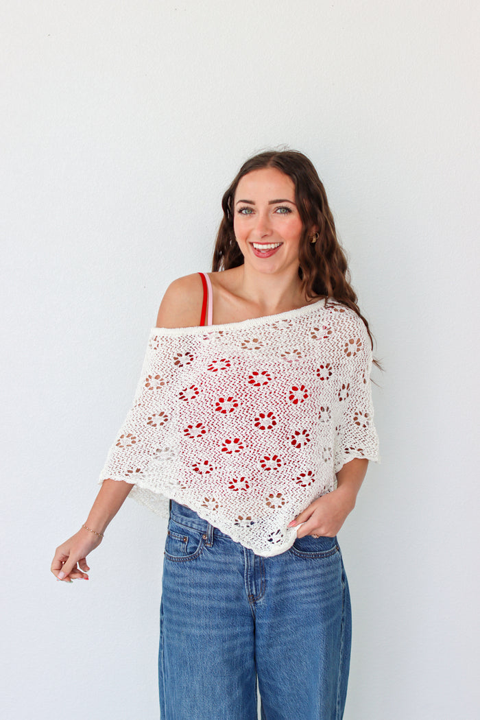 Woman wearing a white crochet shawl with patterns against a plain background