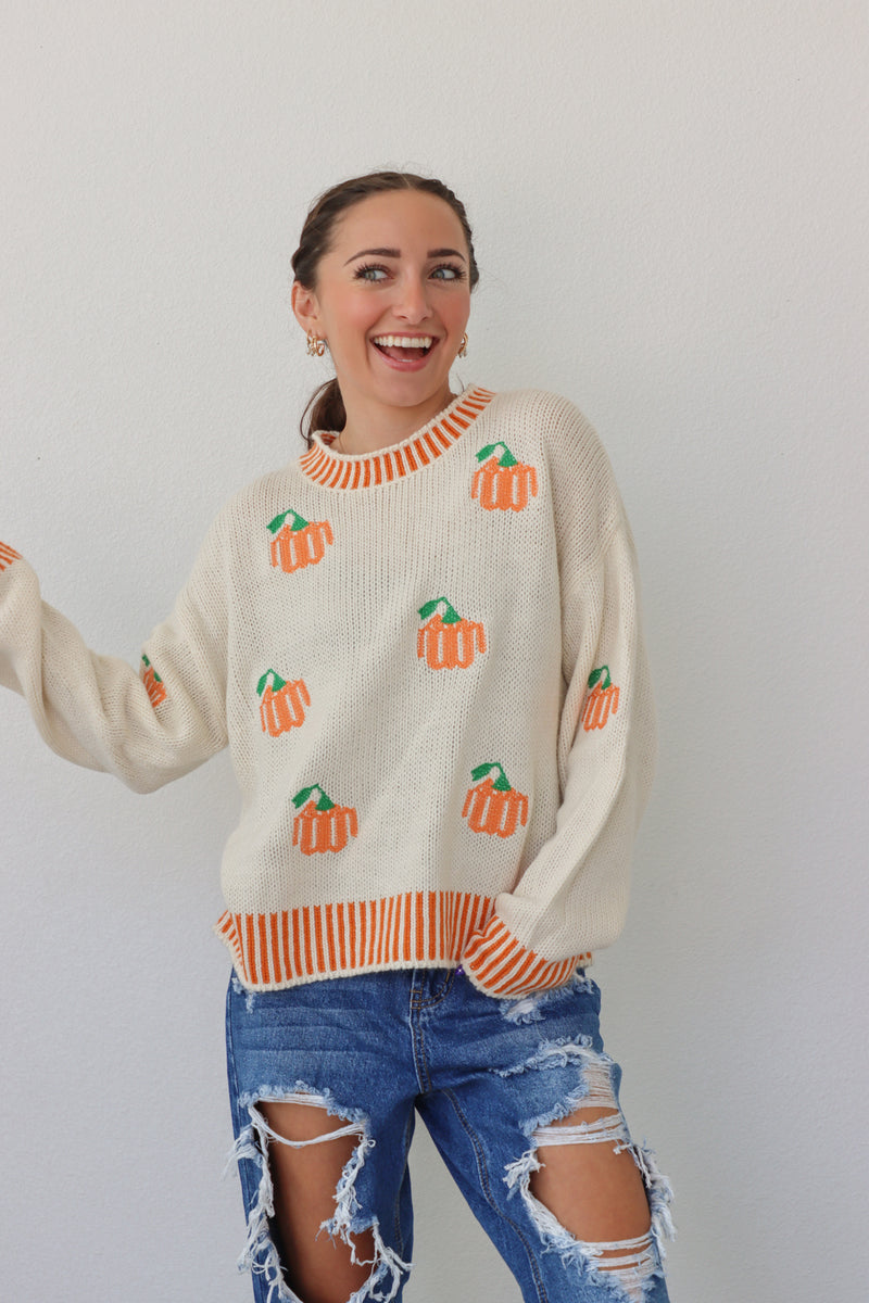 girl wearing cream sweater with orange pumpkin design