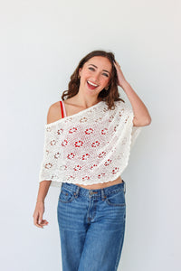 Woman wearing a white crochet shawl with patterns against a plain background