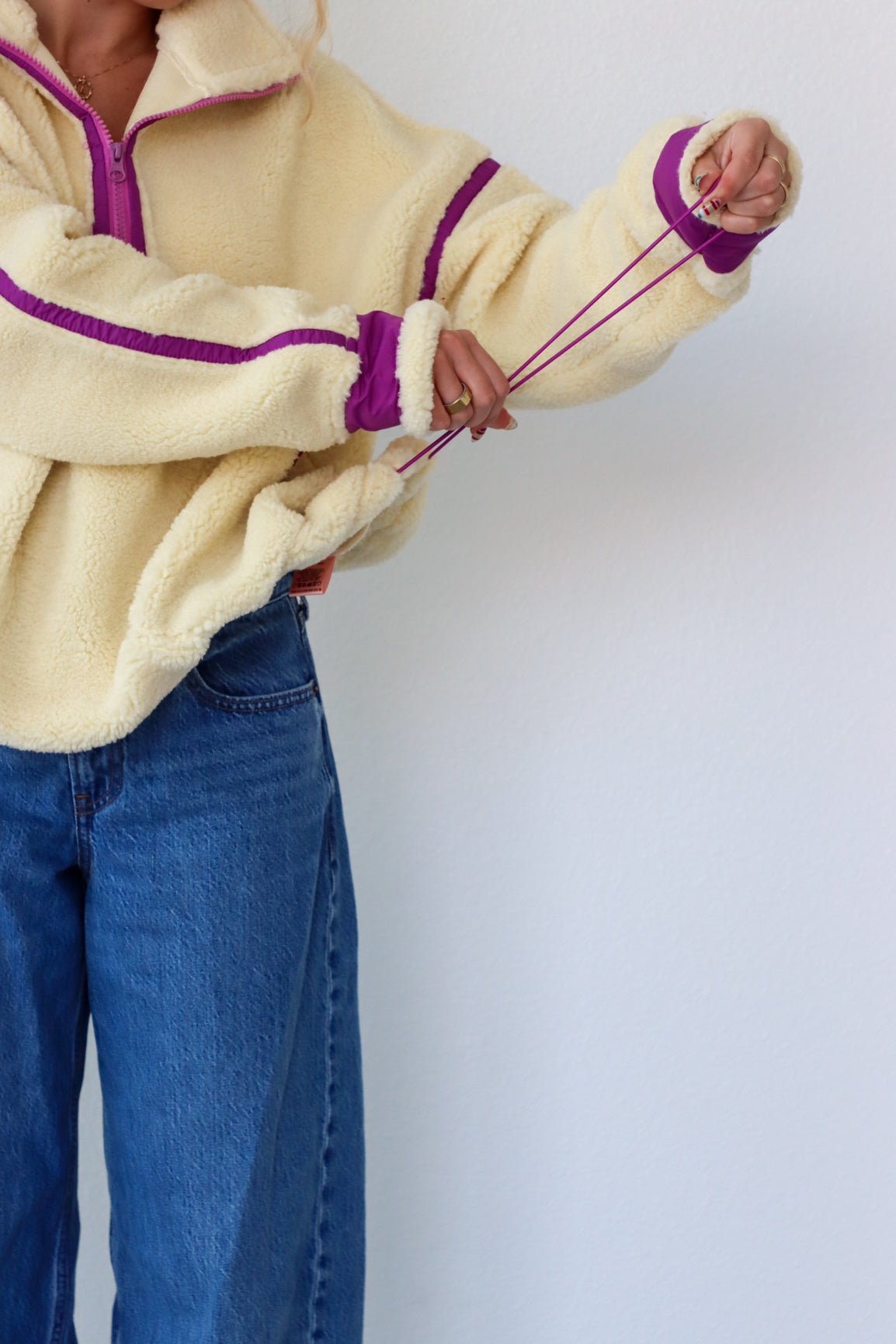 Person wearing a cream fleece jacket with purple accents and blue jeans against a white background