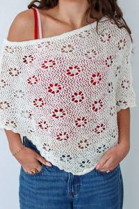 Woman wearing a white crochet shawl with patterns against a plain background