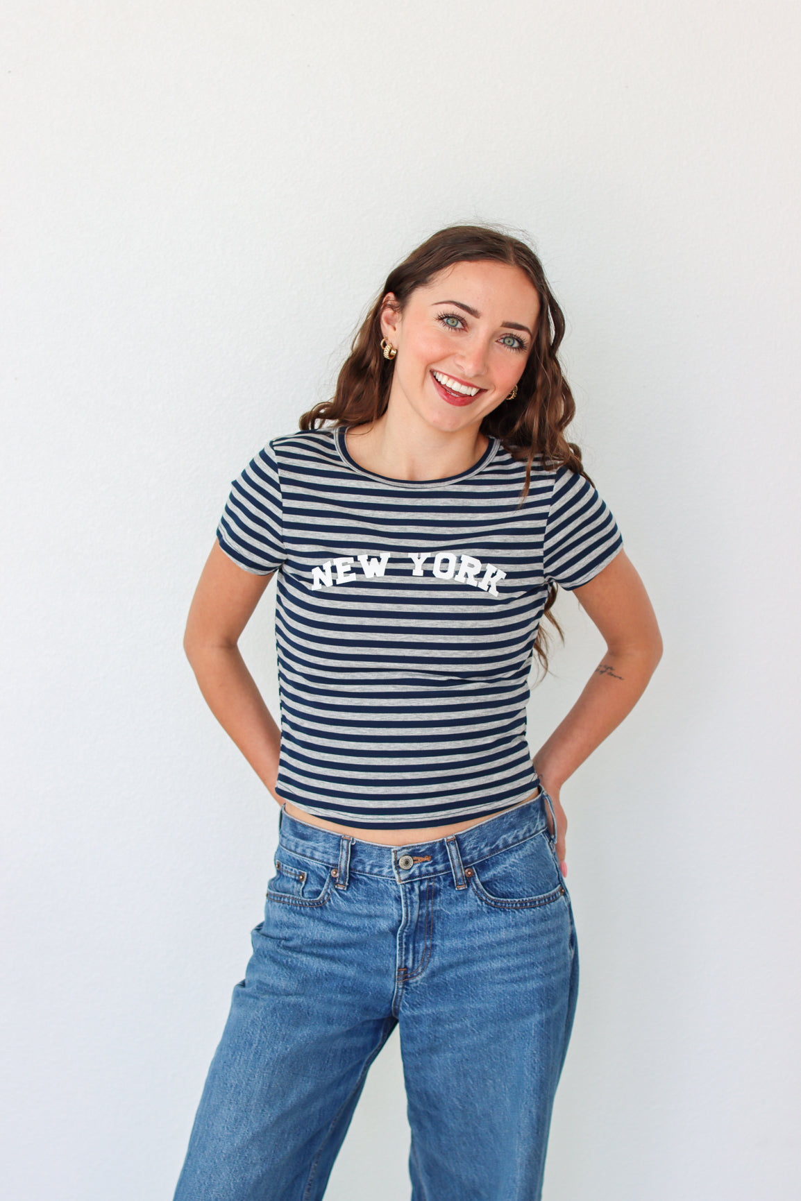 Woman wearing a striped 'New York' t-shirt and blue jeans against a white background