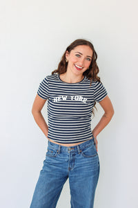 Woman wearing a striped 'New York' t-shirt and blue jeans against a white background