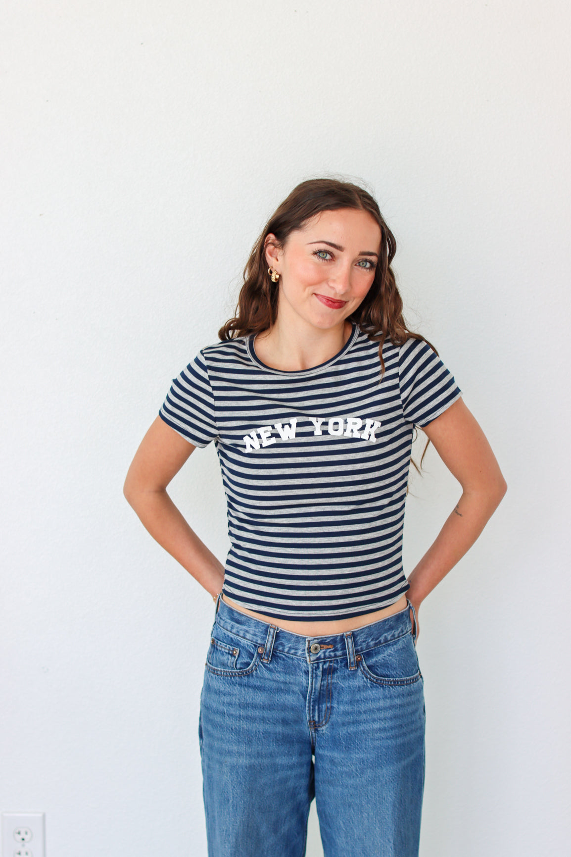 Woman wearing a striped 'New York' t-shirt and blue jeans against a white background