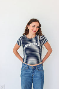 Woman wearing a striped 'New York' t-shirt and blue jeans against a white background