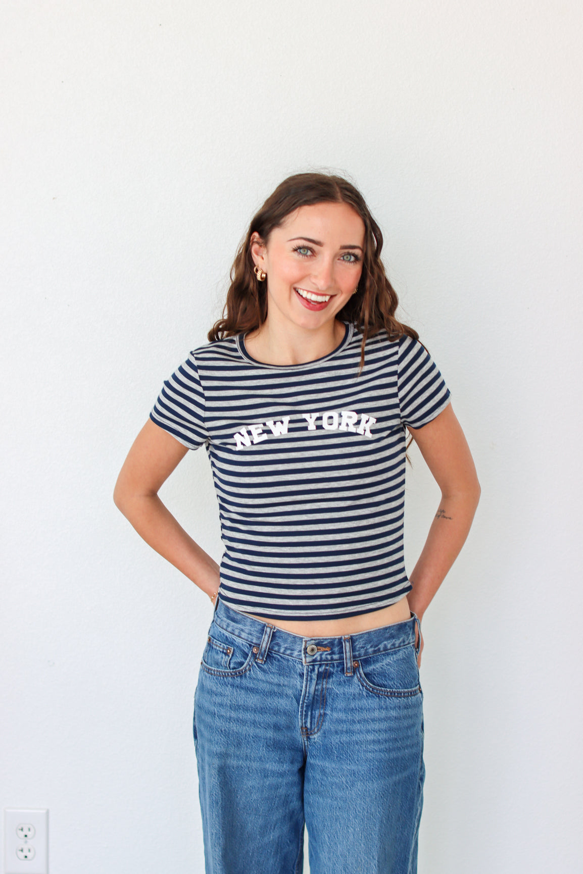 Woman wearing a striped 'New York' t-shirt and blue jeans against a white background
