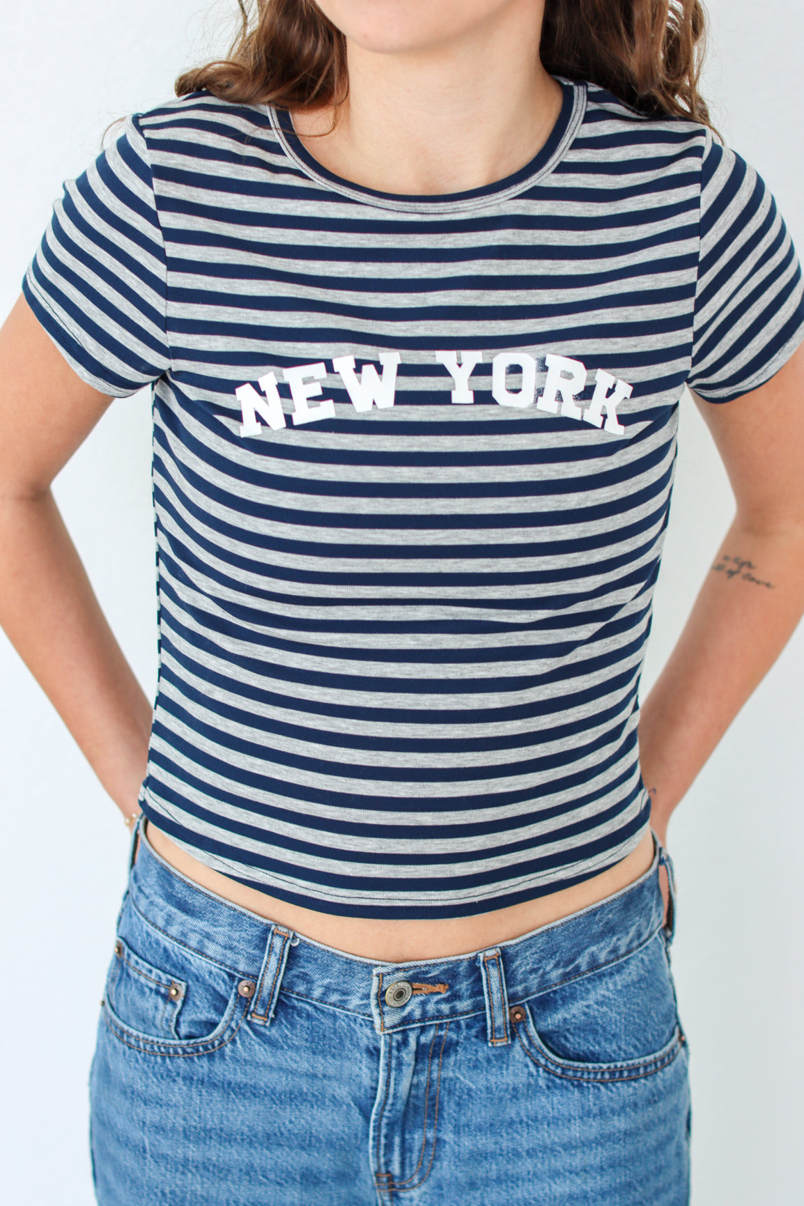 Woman wearing a striped 'New York' t-shirt and blue jeans against a white background