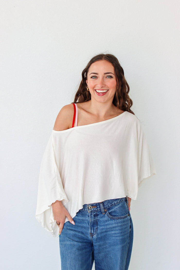 Woman wearing a white off-shoulder top and blue jeans against a white background