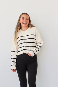 girl wearing cream cable knit sweater with black stripes