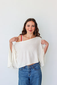 Woman wearing a white off-shoulder top and blue jeans against a plain background