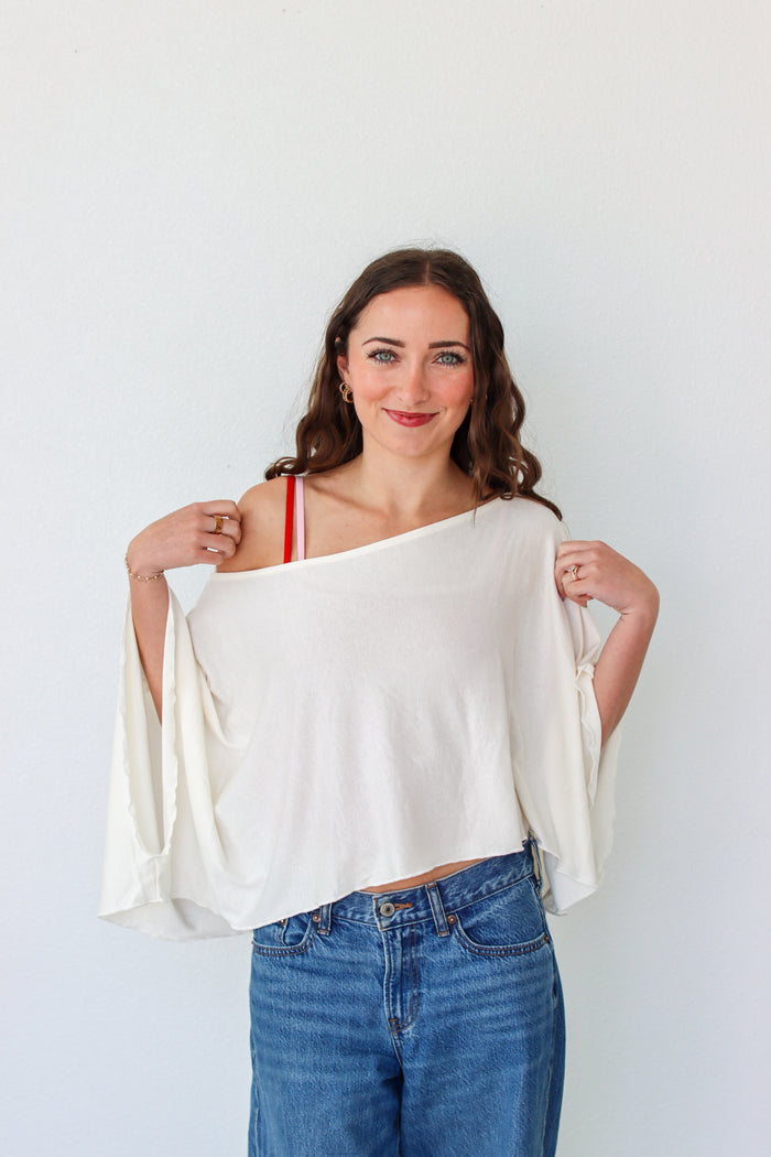 Woman wearing a white off-shoulder top and blue jeans against a plain background