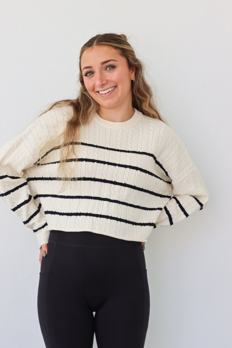 girl wearing cream cable knit sweater with black stripes