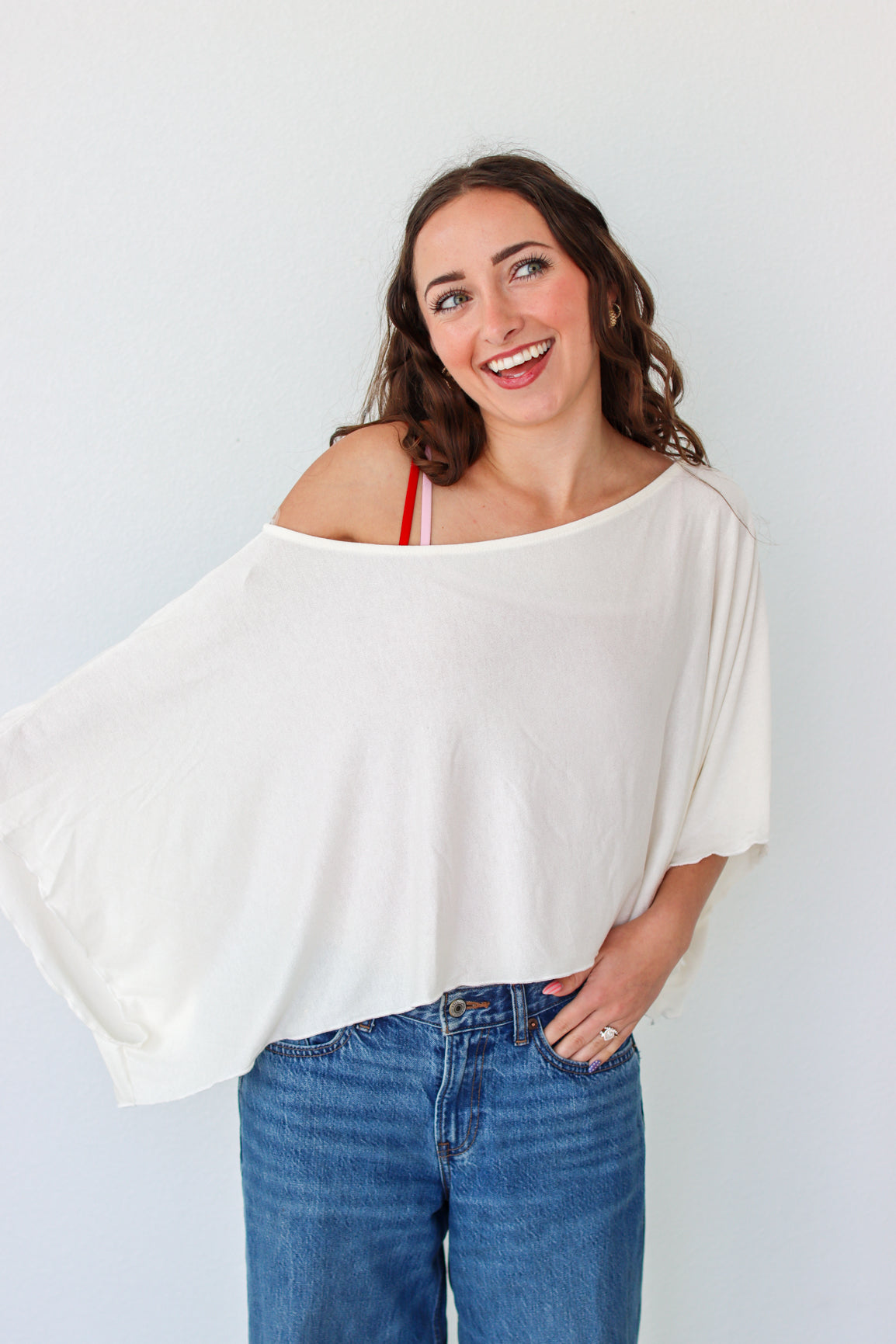 Woman wearing a white off-shoulder top and blue jeans against a light background