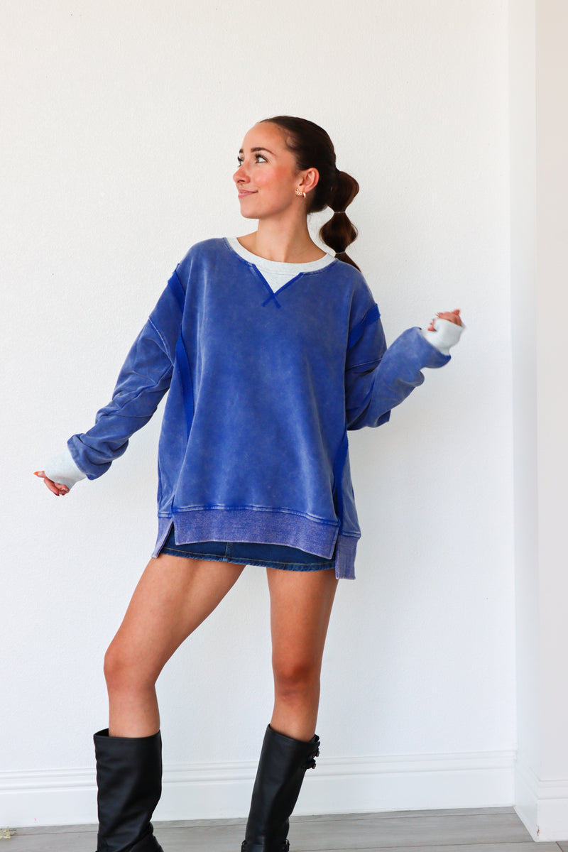 Woman wearing a blue oversized sweater and black boots against a white wall