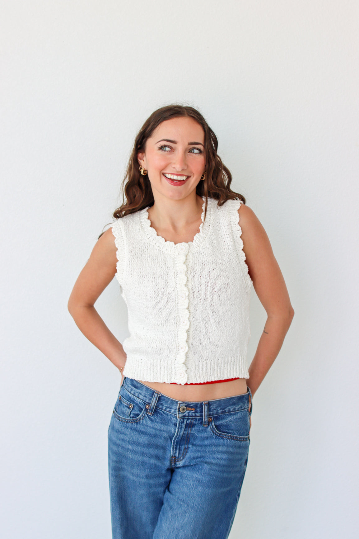 Woman wearing a white sleeveless top and blue jeans against a white background