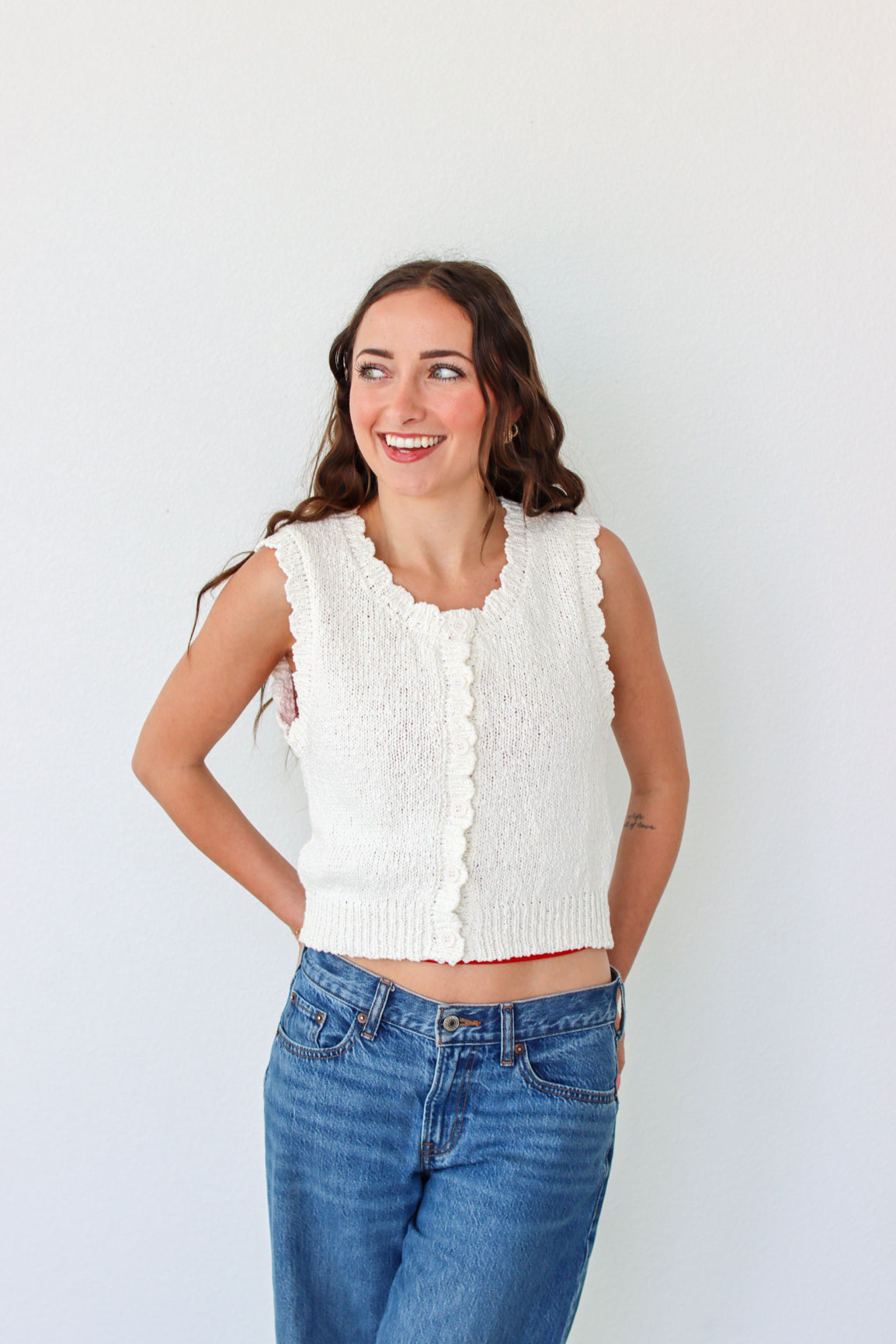 Woman wearing a white sleeveless top and blue jeans against a white background