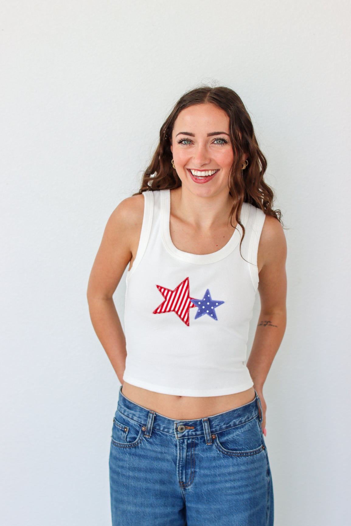 Woman wearing a white tank top with star designs against a plain background