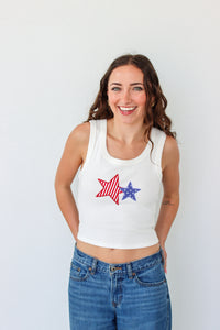 Woman wearing a white tank top with star designs against a plain background