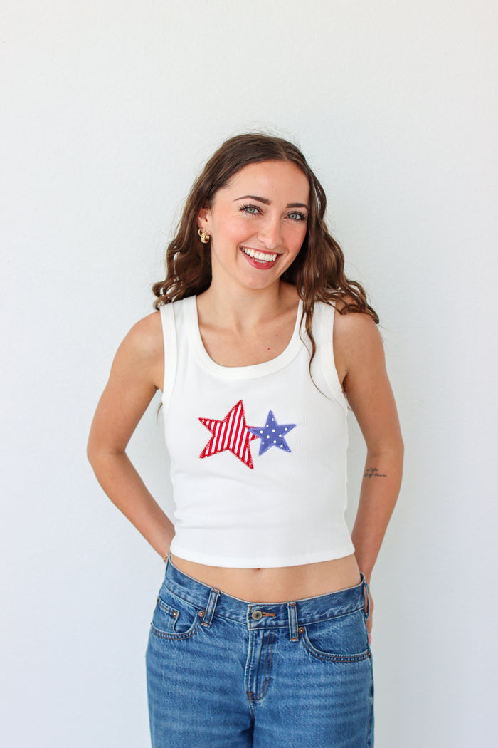 Woman wearing a white tank top with star designs on a plain background