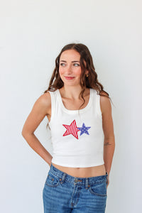 Woman wearing a white tank top with a star design on a plain background