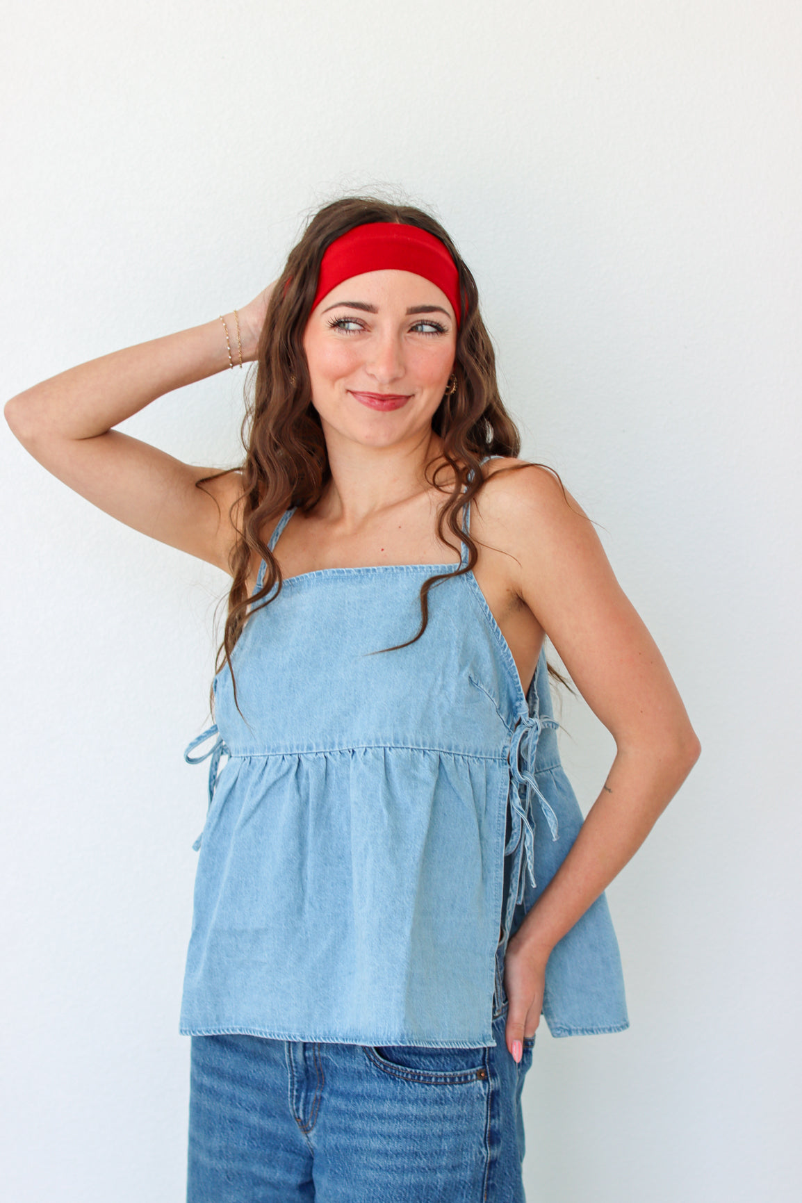 Woman wearing a light blue denim top and jeans with a red headband against a white background