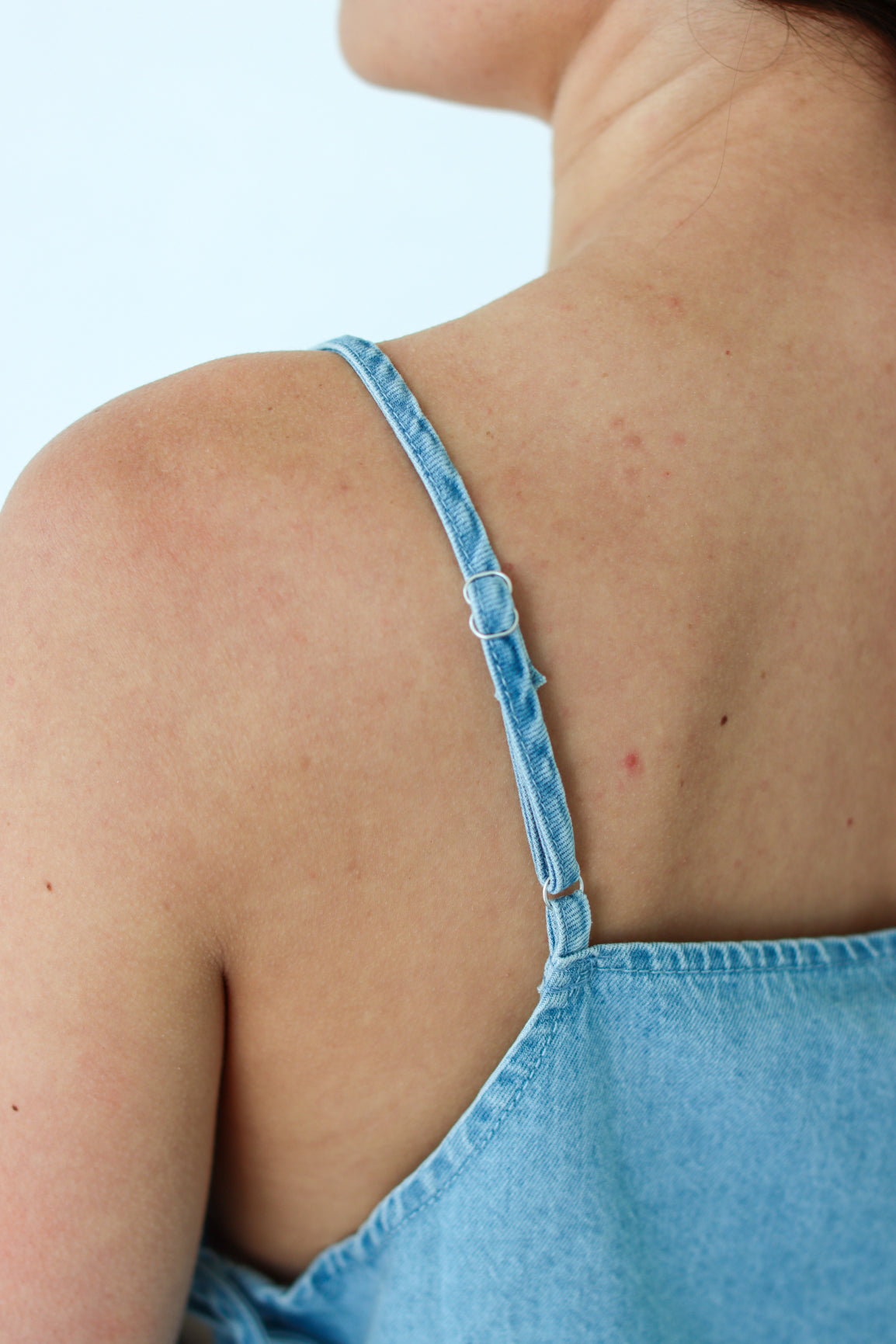 Close-up of a person wearing a blue denim dress with thin straps.